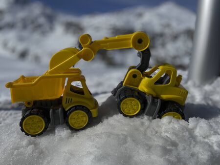 Toy trucks and excavators in the snow in front of a snowy mountain in the Swiss Alps on a sunny winter dayの写真素材