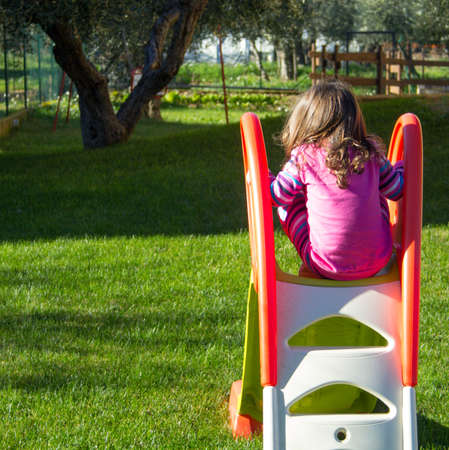 Little girl playing on a children's playground in the shade of an olive treeの写真素材