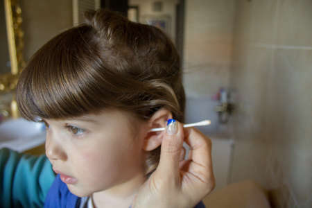 Little girl in the bathroom at home while her mother cleans her ears with a cotton swab. Cleaning children's earsの写真素材