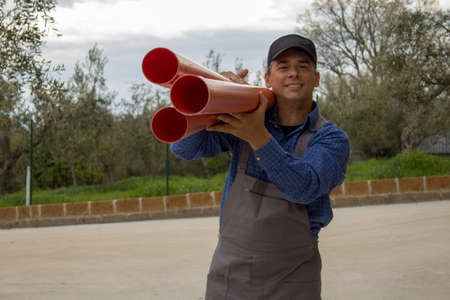 Smiling plumber wearing overalls, while hauling pipes to make a sewer systemの写真素材
