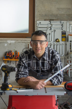 Smiling carpenter handyman in his workshop leaning on a saw bench.の写真素材