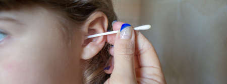 Hands of a mother who cleans her little daughter's ears with a cotton swab. Hygiene teaching. Horizontal bannerの写真素材