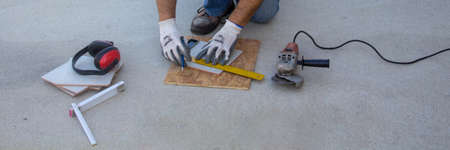 Hands of a bricklayer with grinder and square takes measurements to cut tiles. Do it yourself work