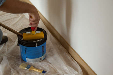 Hand of a painter wetting brush in paint bucket while painting a house wall