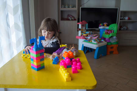 Adorable little girl sitting on a small table playing with colorful constructions.の写真素材