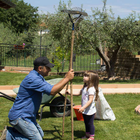 Picture of a gardener dad with his daughter in the backyard while they aerate and collect the leaves...