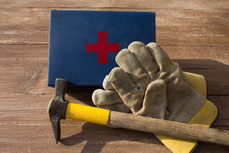 Image of a pair of work gloves, a mason's hammer and a first aid kit. Reference to accidents at work