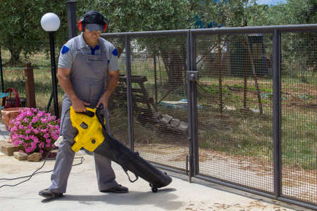 Picture of a handyman gardener sweeping leaves from a garden with a leaf blower