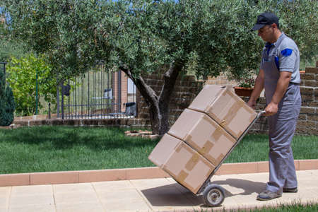 Image of a delivery boy carrying large packages with a trolley at a houseの写真素材