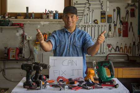Handyman man with thumbs up in his workshop with work tools in front and I can fix it sign related...