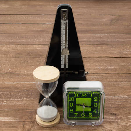 Image of a table clock an hourglass and a metronome, representation of the passing of time.