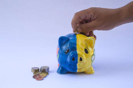 Image of a hand inserting coins into a pig shaped piggy bank. Reference to saving moneyの写真素材