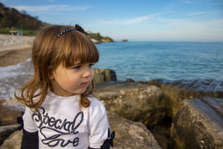 Picture of an adorable little girl sitting on a cliff by the sea in spring during a vacation in Italy on the trabocchi coastの写真素材