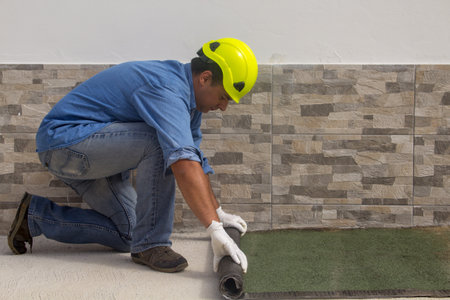 Construction worker at work while unrolling the tarred bituminous sheath to protect roofs and floors from bad weather and rain. Insulation in the construction sector.の写真素材