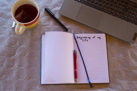Image of an open diary with the heading Beginning of my life, with a blank page to insert text, a pen and a laptop.の写真素材