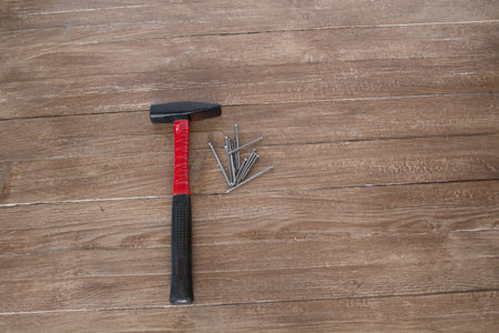 Image of a hammer with nails at its side resting on a wooden planks background.