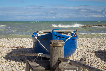 Image of a pulley winch for towing a blue boat on the rough seashoreの写真素材