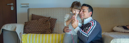 Image of a smiling dad hugging his daughter as they play house and sing karaoke. Horizontal bannersの写真素材