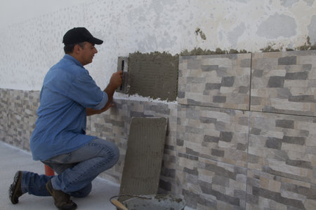 Image of a handyman tiler who with a spatula spreads the glue for laying the tiles on a house wall. Do-it-yourself work and home renovation.の写真素材