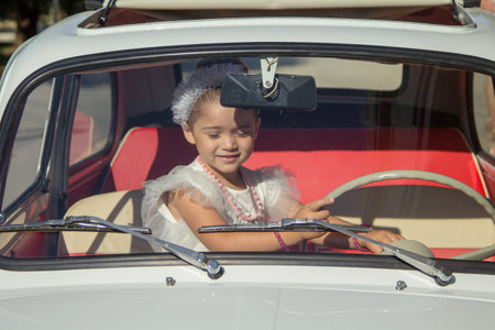 Image of an adorable little girl playing inside an old historic Italian car at a ceremonyの写真素材