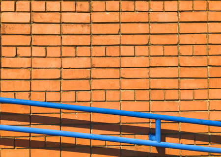 Orange brick wall. Textured background with copy space for design work. Material pattern. Reddish-brown brick blocks facade with blue handrail. Industrial wallpaper with brickwork. No people.の写真素材