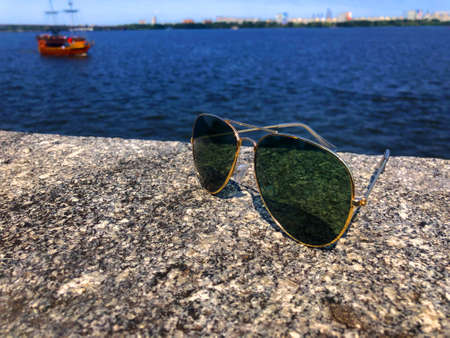 Fashionable aviator sunglasses with dark lenses and gold frames sit on a granite stone pier and...