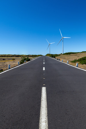 a straight road with two wind turbines over the area with a blue skyの写真素材