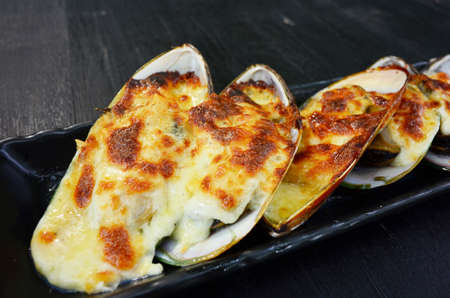 Mussels baked with cheese on black plateの写真素材