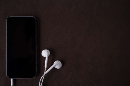 Dark concept black hand phone with earphone	 on leather backgroundの写真素材