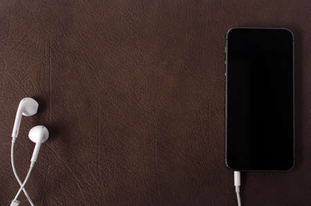 Dark concept black hand phone with earphone	 on leather backgroundの写真素材