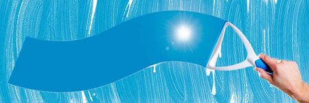 Hand With Squeegee Cleaning Soapy Window With Blue Sky And Sun Shining Through