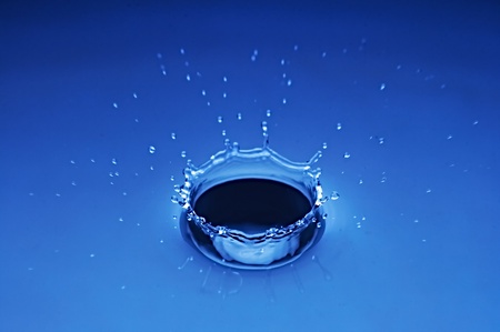 tumbled drop of water with splashes on turn blue backgroundの写真素材