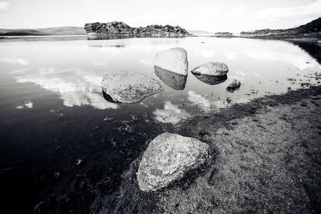 Blue lake idill under cloudline sky with rocks and stones monochromeの写真素材