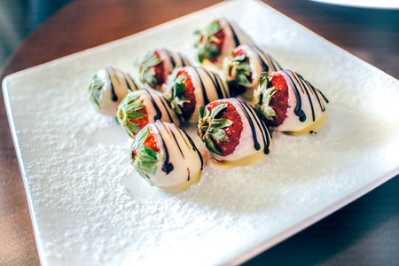 Close up white chocolate strawberry with dark chocolate decoration and sugar powder  on the white plateの写真素材