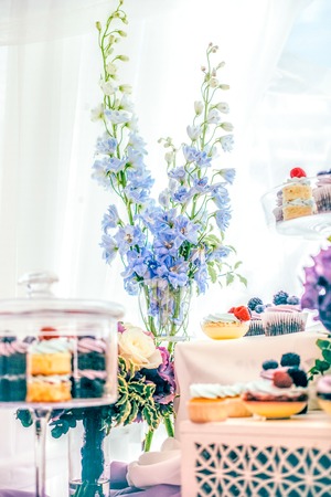 Blue flowers and cupcakes with berries with the glass cloche bell with pedestale on the violet tablecloth decorationの写真素材