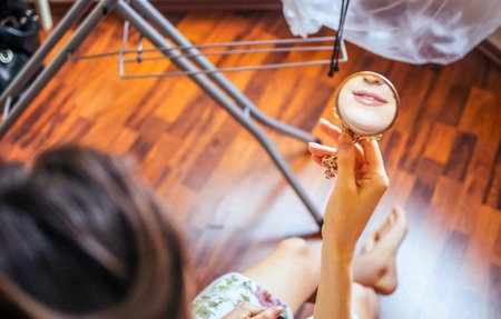 Girl smiling in the mirror during the wedding preparation, wooden floor and other bride elements on the backgroundの写真素材