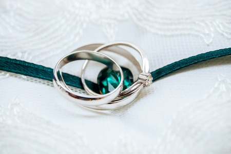 Close-up wedding white-gold ring with diamond and emerald ribbon on the white lacy pillowの写真素材