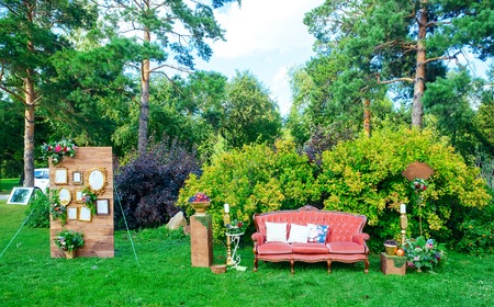 White wooden seat decorated for wedding by colorful throw pillows with round, romb and heart shape on the green lawn with different flower compositionsの写真素材