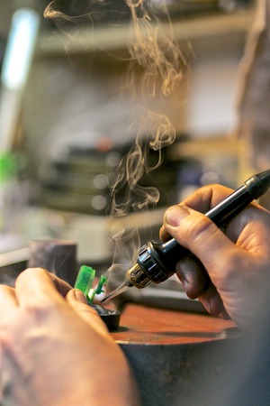 man soldering the ring by hands with some smoke on background at jewelry workshop