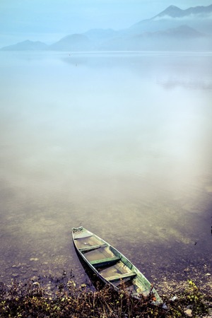 Lonely fishing boat on the lakeside with for and voilet-blue color verticalの写真素材