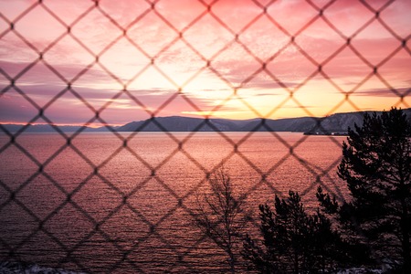 Sunset through the  metal-mesh fence with mountain view and pinkcoloredの写真素材