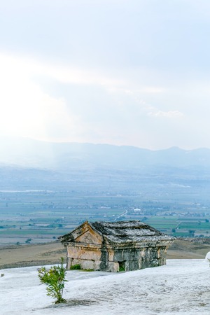 Stone-house on the peak of white travertine hill with blurred town on background wallpaper - Pamukkaleの写真素材