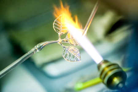 Artist shaping hot glass into a figurine, using a gas flame.