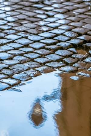 lantern reflection in a puddle on road from stone blocks