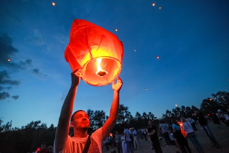Omsk, Russia - June 16, 2012: festival of Chinese paper lantern, the man starts lantern in the sky at nightのeditorial素材