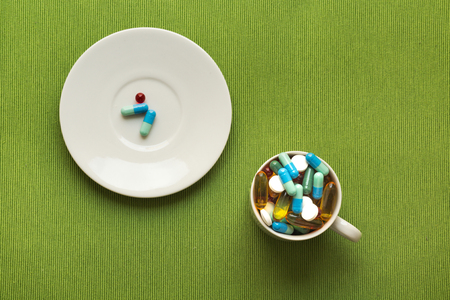colorful medical pills on white saucer and cup on green backgroundの写真素材