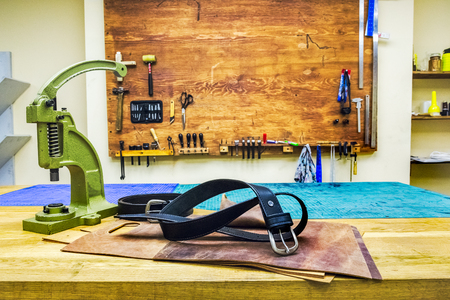 leather workshop black belt and grips on table in front of wodden board with tools