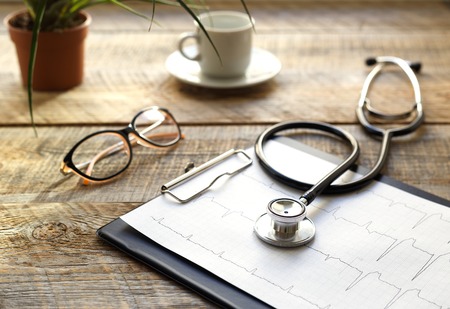 doctor workplace with a stethoscope, glasses and coffe cup at wooden tableの写真素材