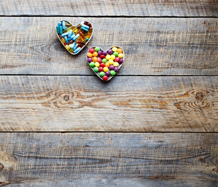 many colorful medical pills in shape of two hearts isolated on wodden tableの写真素材
