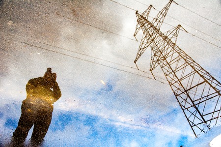Photographer reflection on a water puddle with blue sky and electric towerの写真素材